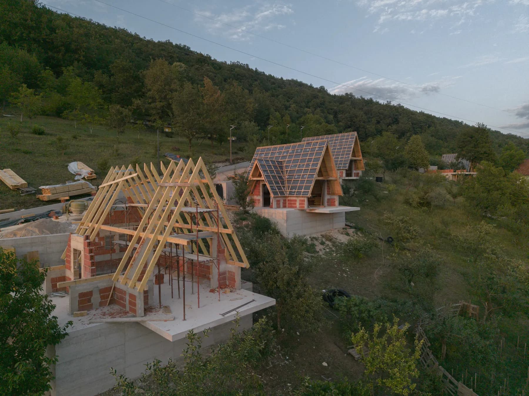 Dvije A-frame vikendice u izgradnji, na prednjoj goli rogovi, na zadnjoj već postavljena krovna oplata